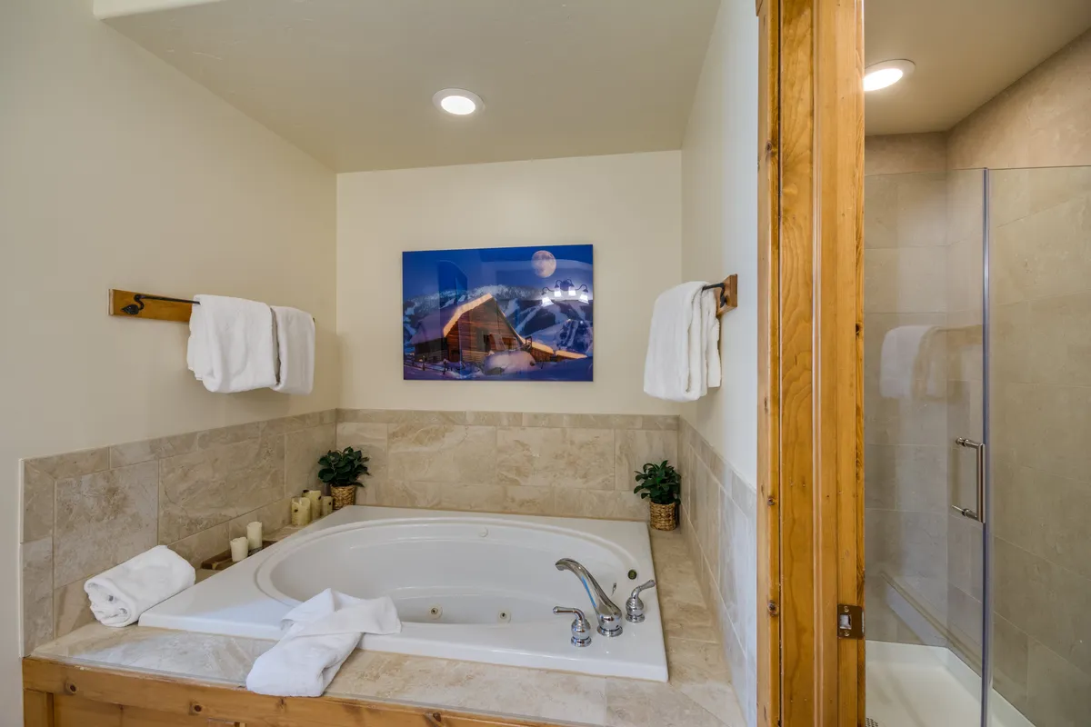 A tranquil ensuite bathroom spotlighting a luxurious soaking jacuzzi tub, artfully placed mountain-themed artwork, fresh towels, and a small potted plant—designed for relaxation and indulgence.
