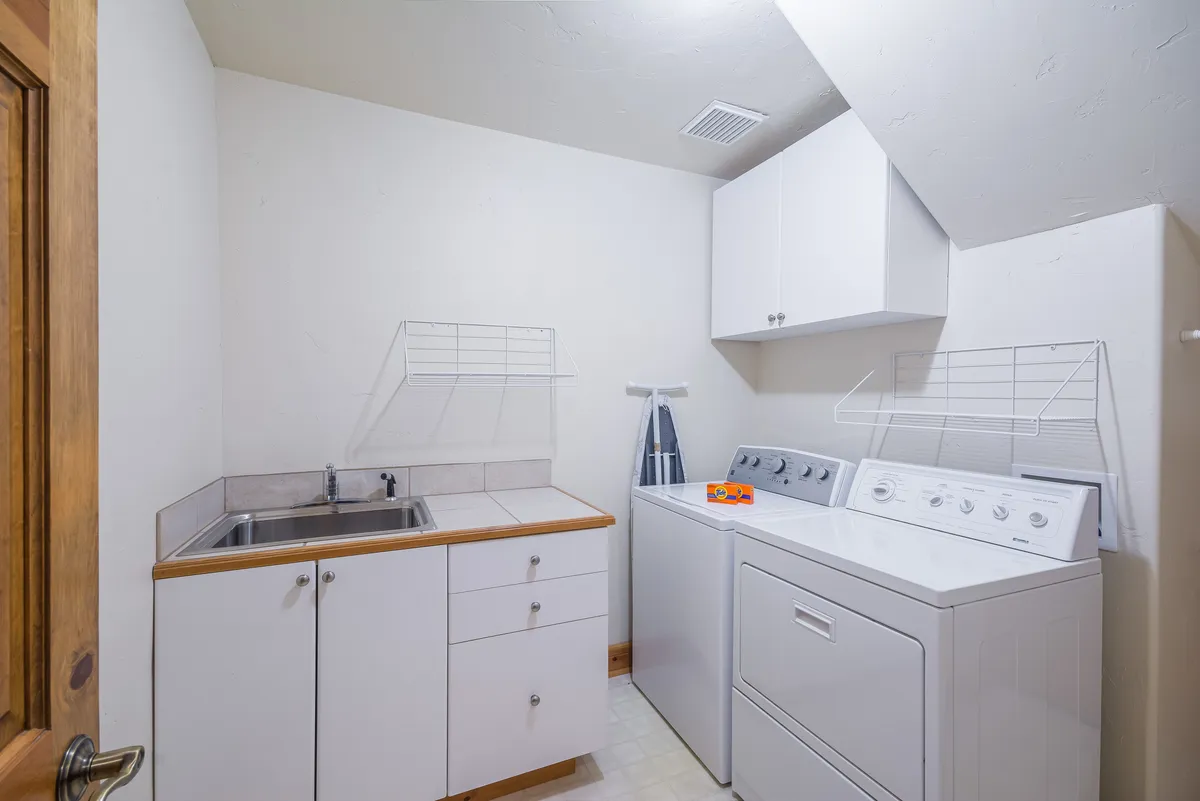 The image showcases a functional laundry area featuring a washing machine, dryer, utility sink, and shelves for storage. The mood is practical and organized, underscoring the home’s readiness for handling gear and clothing after a day outdoors.