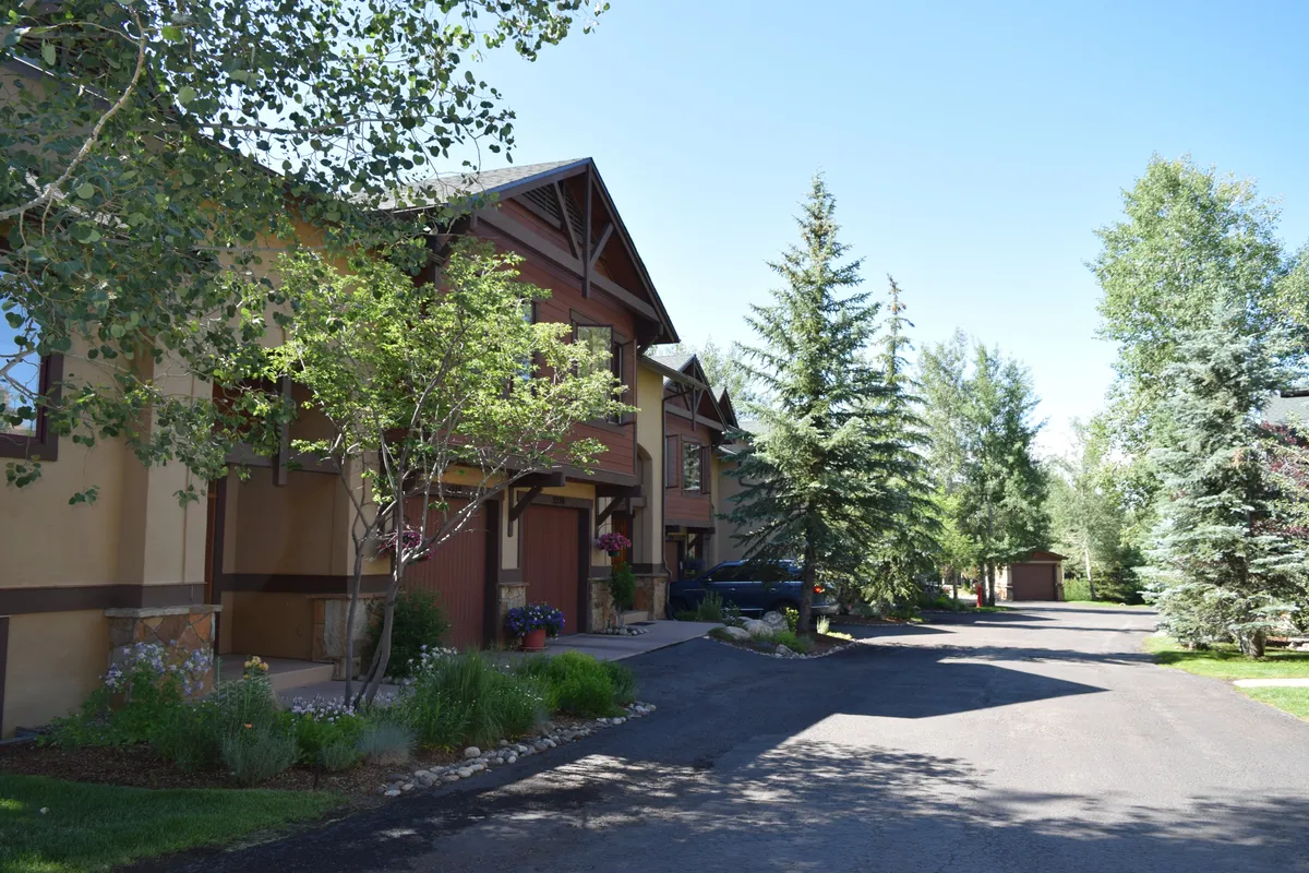 This image displays a row of charming townhouses bordered by lush greenery and a well-maintained pathway. The inviting scene suggests ease of access to walking trails and community spaces, with mature trees providing shade and a sense of summer vibrancy.