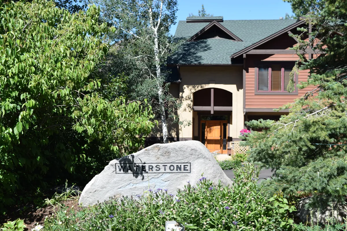A welcoming exterior view of the townhome community's entrance, featuring a prominent stone sign reading 'WATERSTONE.' Lush greenery and the inviting main pathway create a tranquil first impression, suggesting easy access to both natural surroundings and resort amenities.