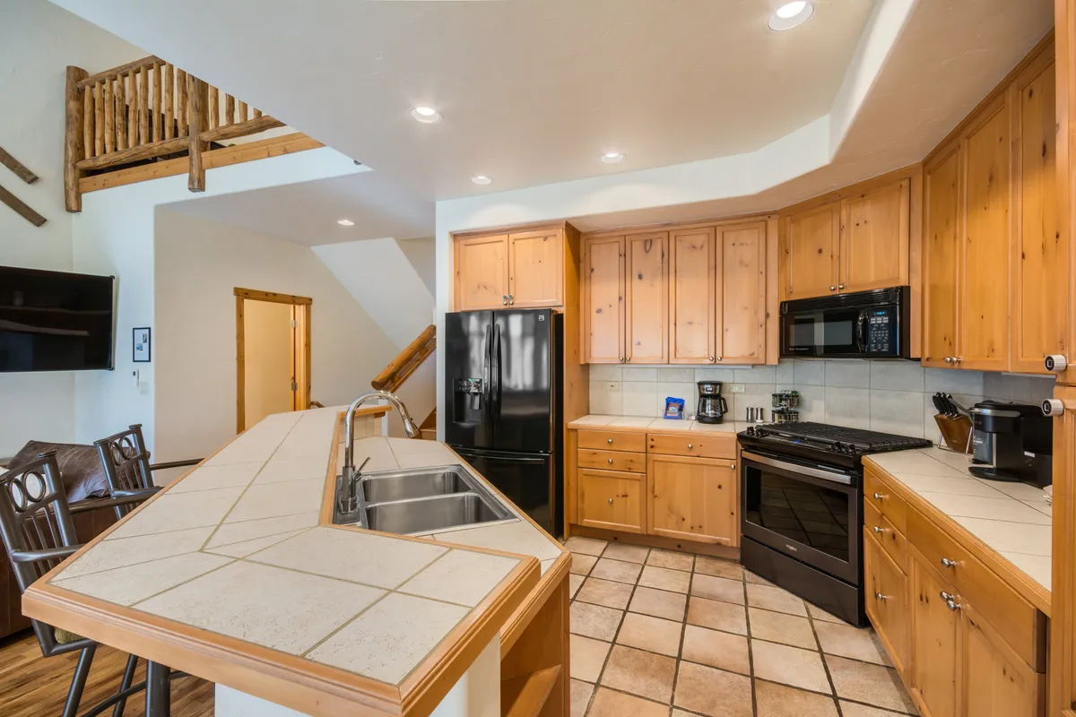 A spacious, well-equipped kitchen with a large island, black refrigerator, warm wooden cabinetry, and stainless steel appliances. The space is well-lit and designed for both cooking and casual dining, fostering togetherness and convenience.