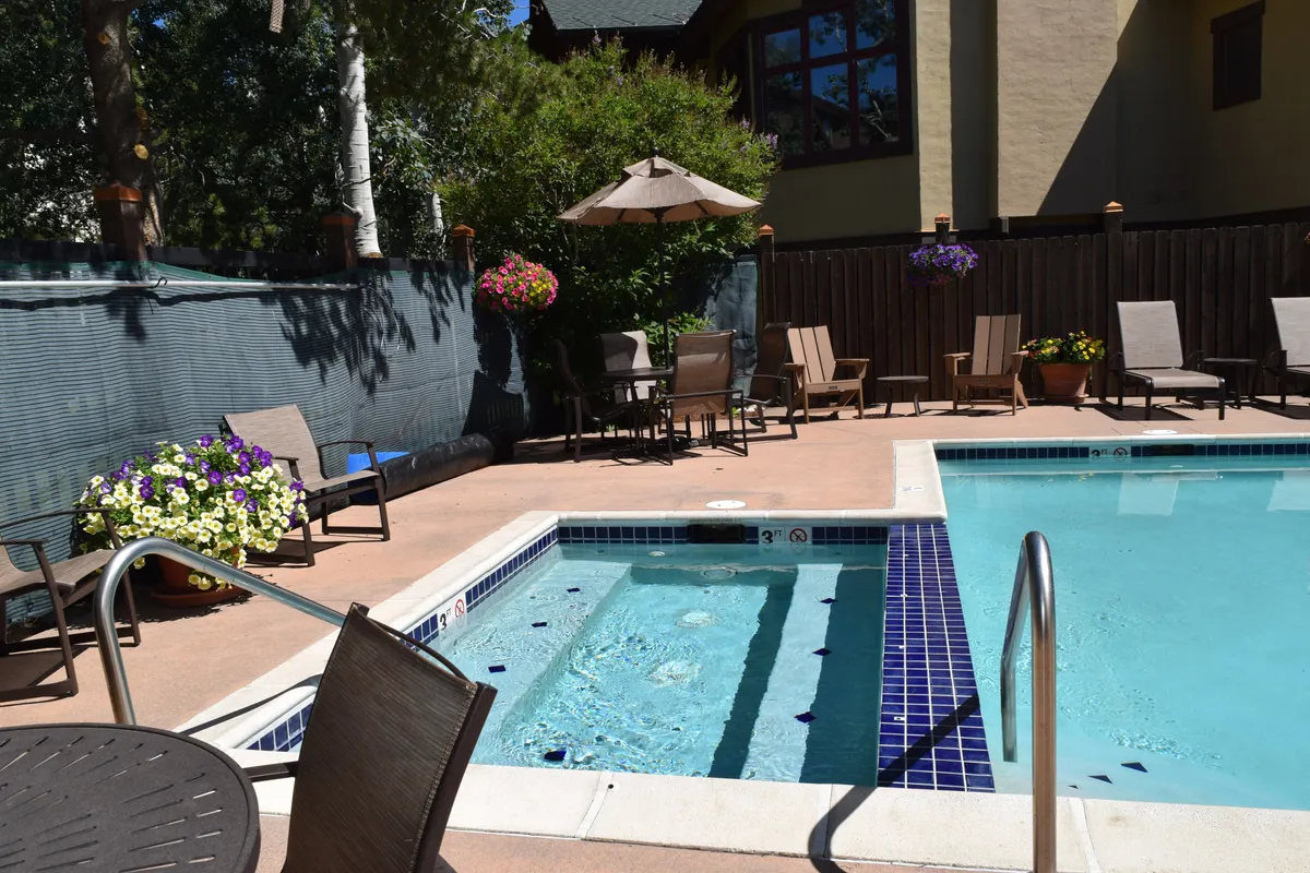 An inviting outdoor heated pool and adjacent hot tub are nestled beside a lush landscape, with lounge chairs and umbrellas providing relaxation spaces around the water. Flower pots add a pop of color, and the tranquil setting creates a resort-like atmosphere perfect for unwinding after a day of adventure.