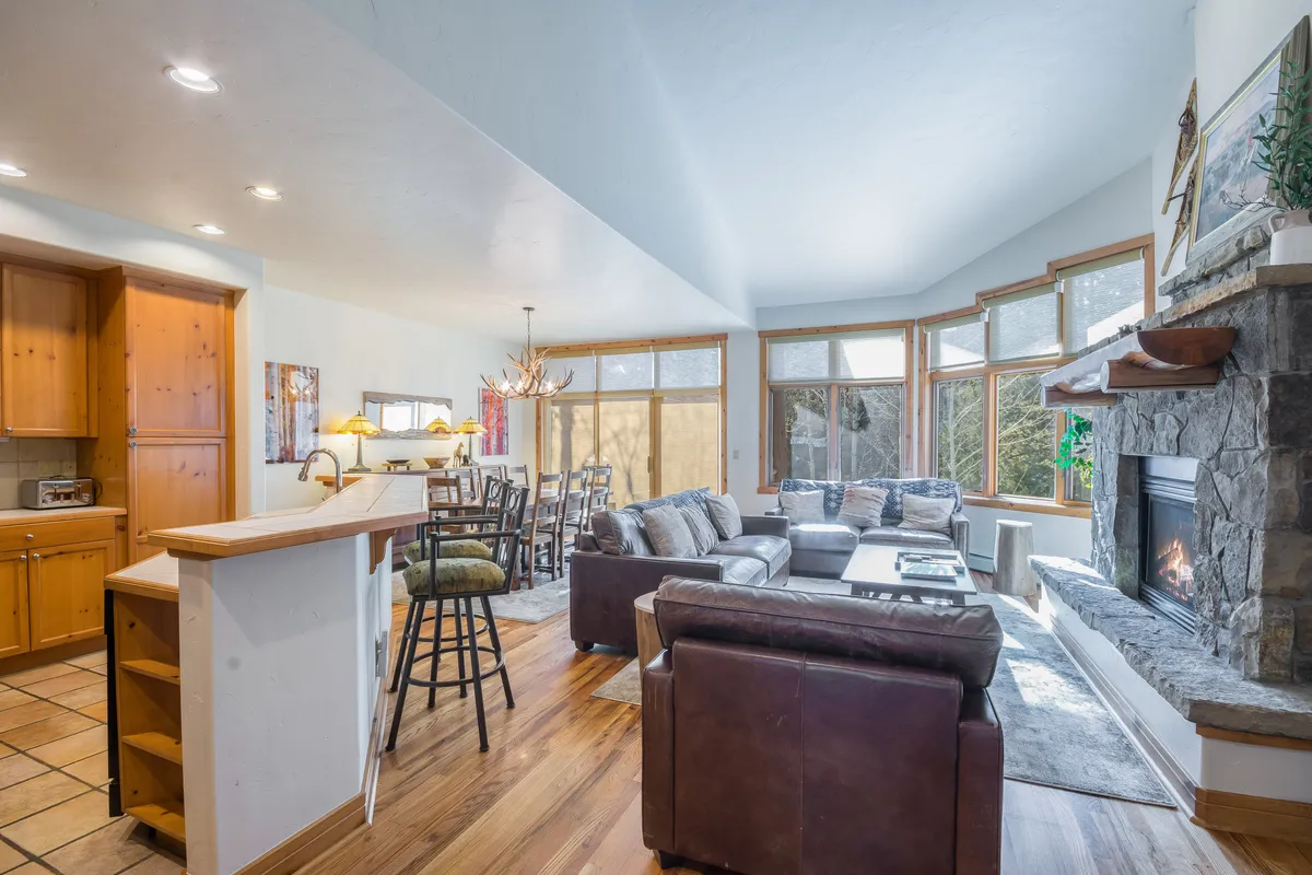 A welcoming open-concept space featuring a gas fireplace, large windows with scenic views, a spacious dining area, and a comfortable sofa arranged for conversation and relaxation. The natural light and connection between living and dining zones create an inviting atmosphere for gatherings.
